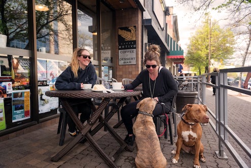 在Kamloops的咖啡店里，两名妇女在户外和狗狗一起喝咖啡